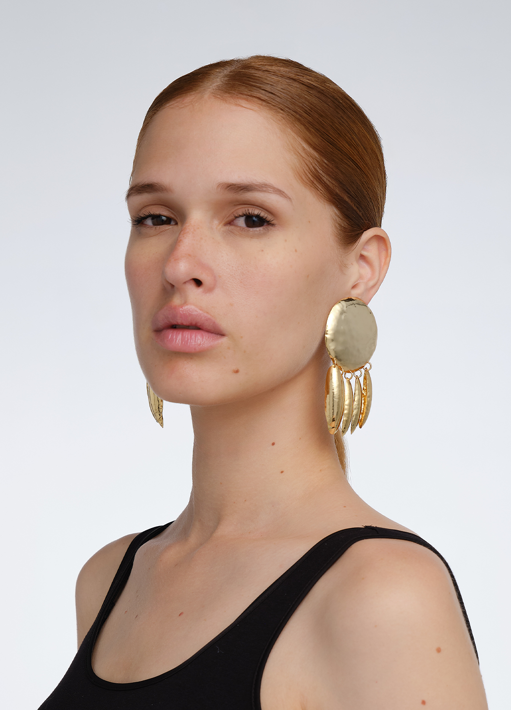 Modelo con look pulido usando aretes medianos en dorado con base circular y colgantes ovalados,
ambos con textura repujada; una pieza de diseño escultórico de Paula Mendoza.