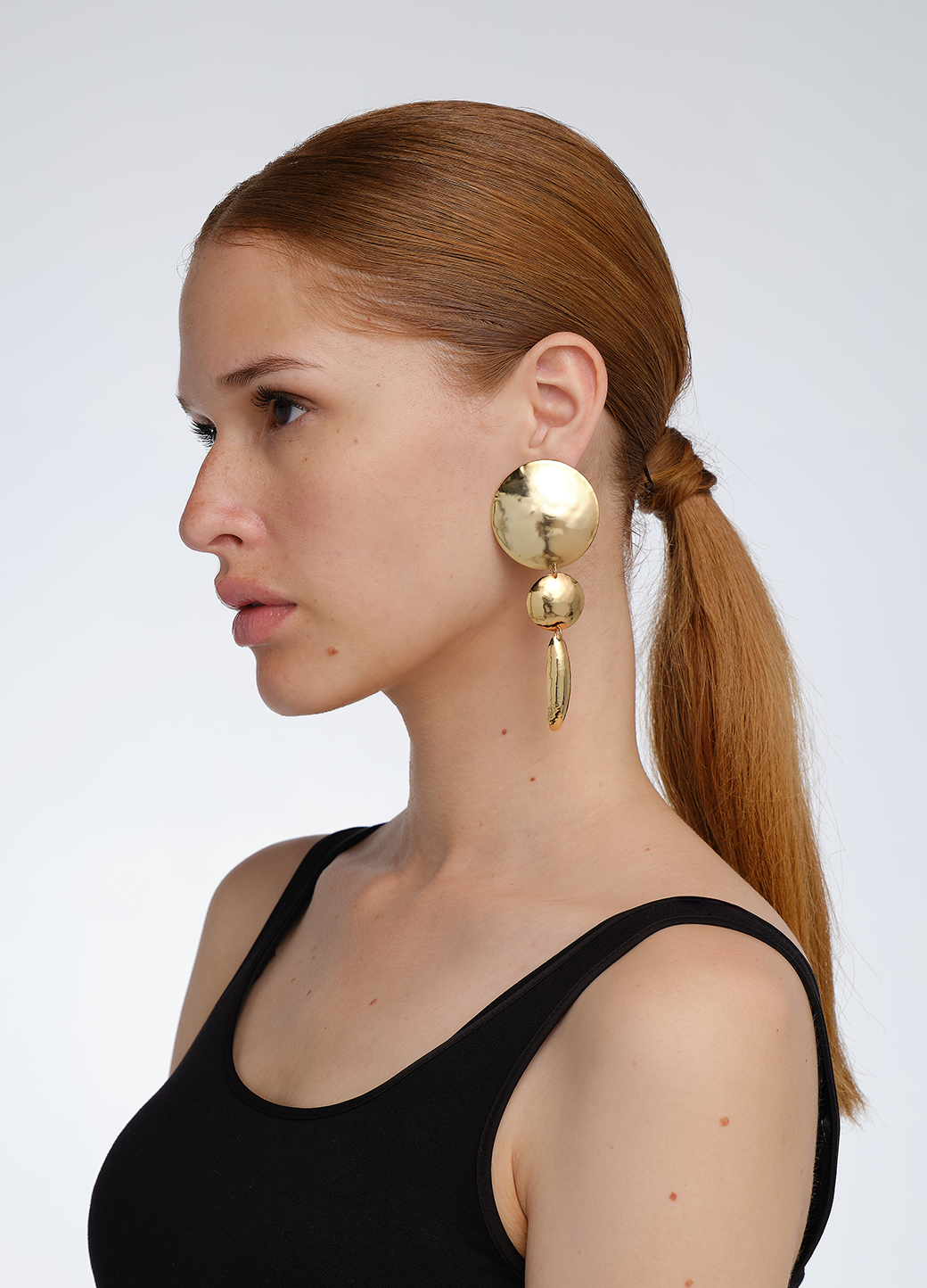 Modelo con look pulido usando aretes medianos y largos en dorado compuestos por dos círculos y un
óvalo, todos con textura repujada; una pieza de diseño escultórico de Paula Mendoza.