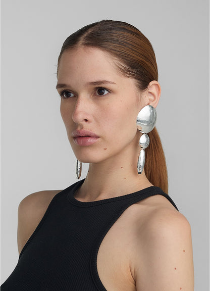 Modelo con look pulido usando aretes grandes y largos en plateado compuestos por dos círculos y un
óvalo, todos con textura repujada; una pieza de diseño escultórico de Paula Mendoza.